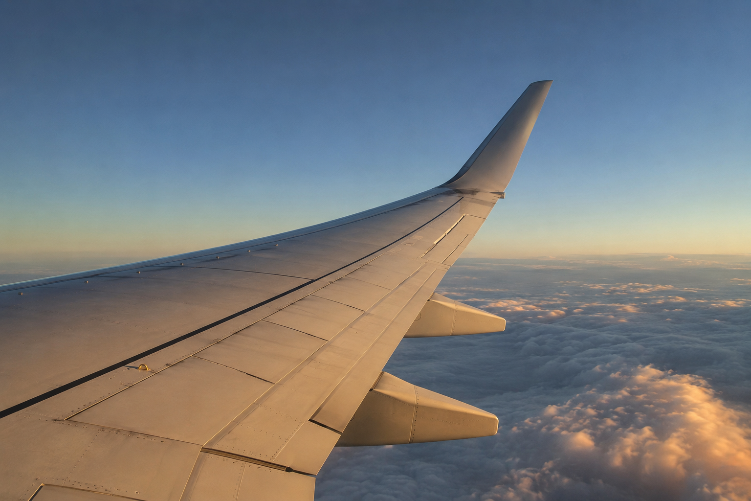 Fluegel eines Airliners im Reiseflug, unter Last nach oben gebogen, Wolkendecke darunter